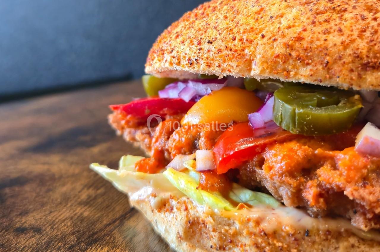 Burger garni de poulet pané, laitue, poivrons, oignons rouges, jalapeños et sauce, sur une table en bois.