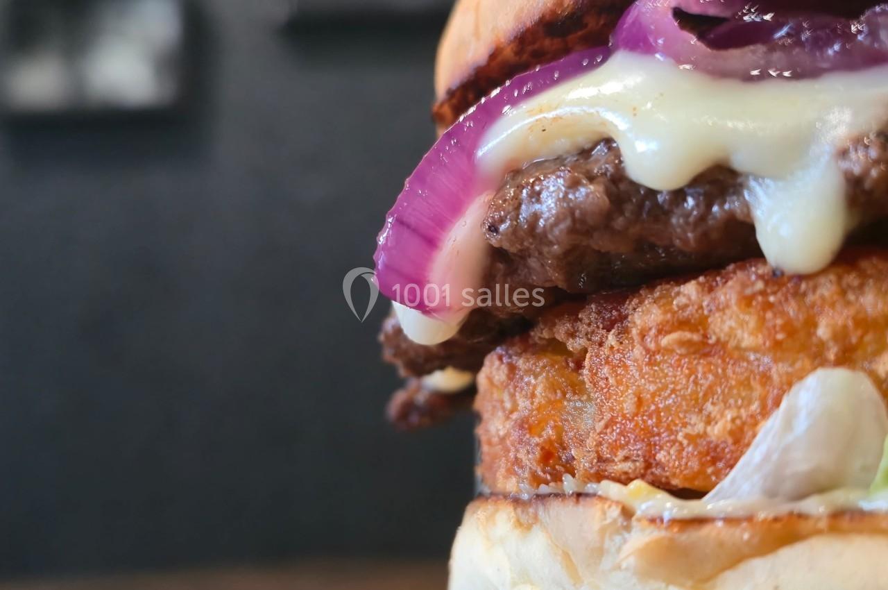 Gros plan d'un burger avec steak, rondelle d'oignon rouge, fromage fondu et galette croustillante.