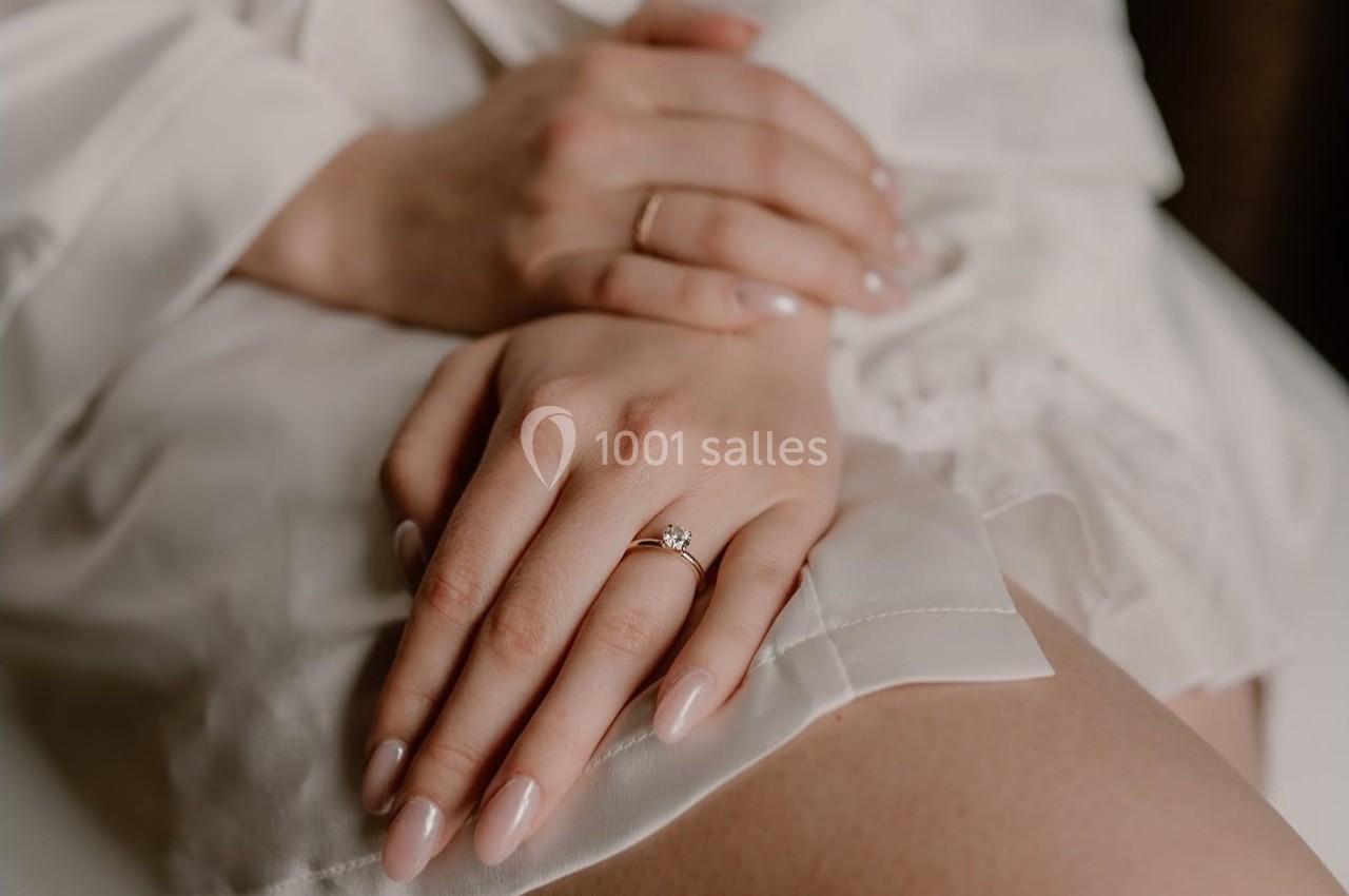 Mains croisées posées sur une robe blanche, mettant en valeur une bague ornée d'une pierre.