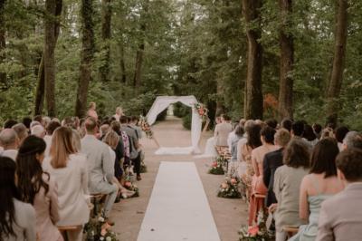Un couple monte des marches, la mariée en robe blanche et voile, entourée d'invités élégamment vêtus.