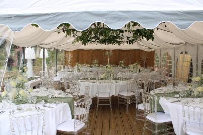 Maison entourée de rosiers et de grands arbres, avec une terrasse couverte et des tables installées à l'extérieur.