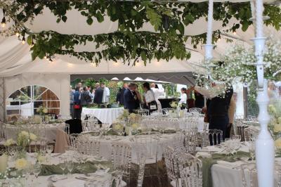 Maison entourée de rosiers et de grands arbres, avec une terrasse couverte et des tables installées à l'extérieur.