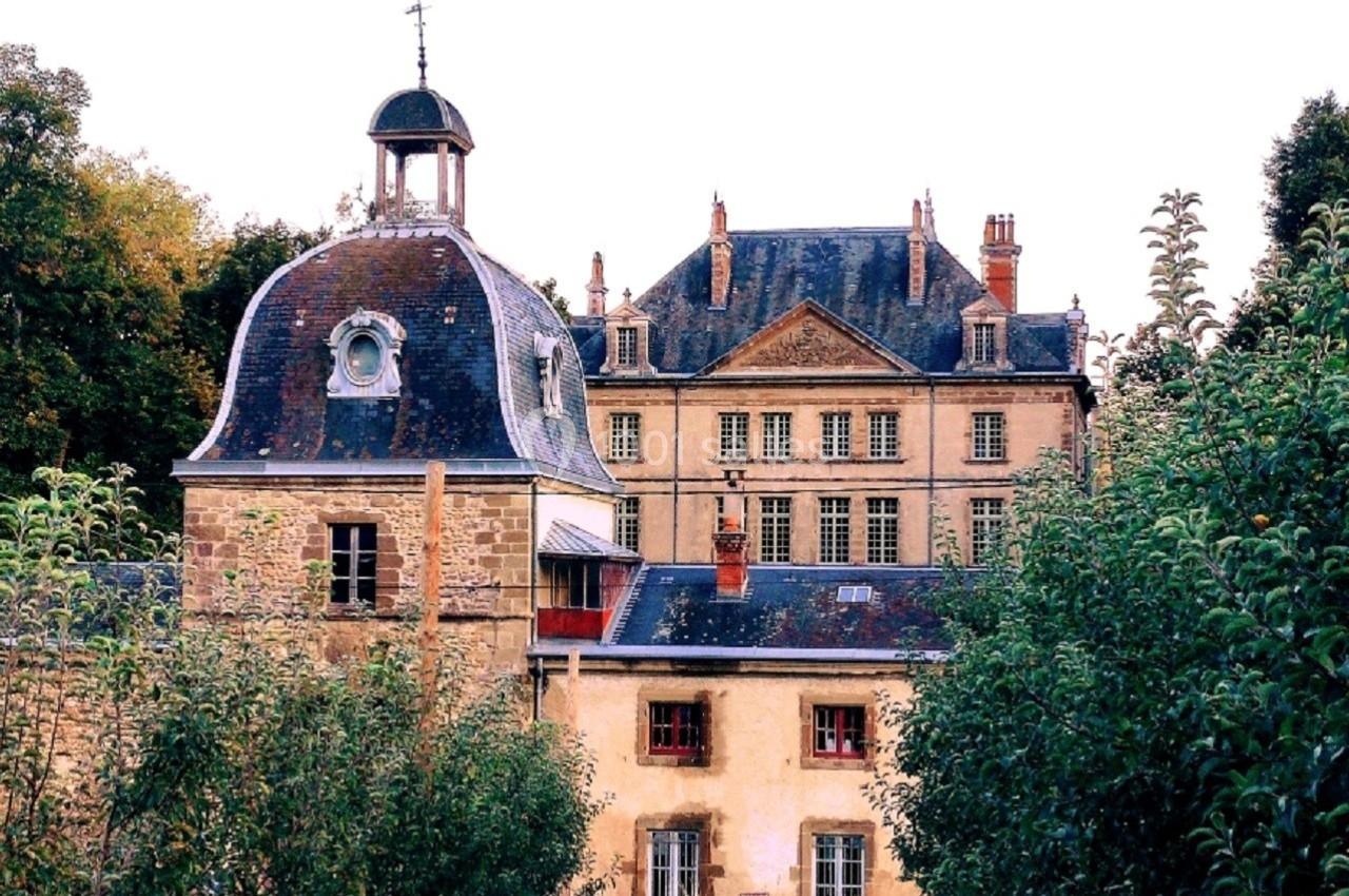 Bâtiment historique en pierre avec une tour à dôme, entouré d'arbres et d'un verger verdoyant.