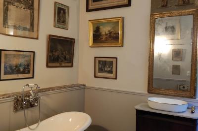 Salle de bain avec baignoire sur pieds, lavabo sur meuble en bois et murs décorés de cadres anciens.