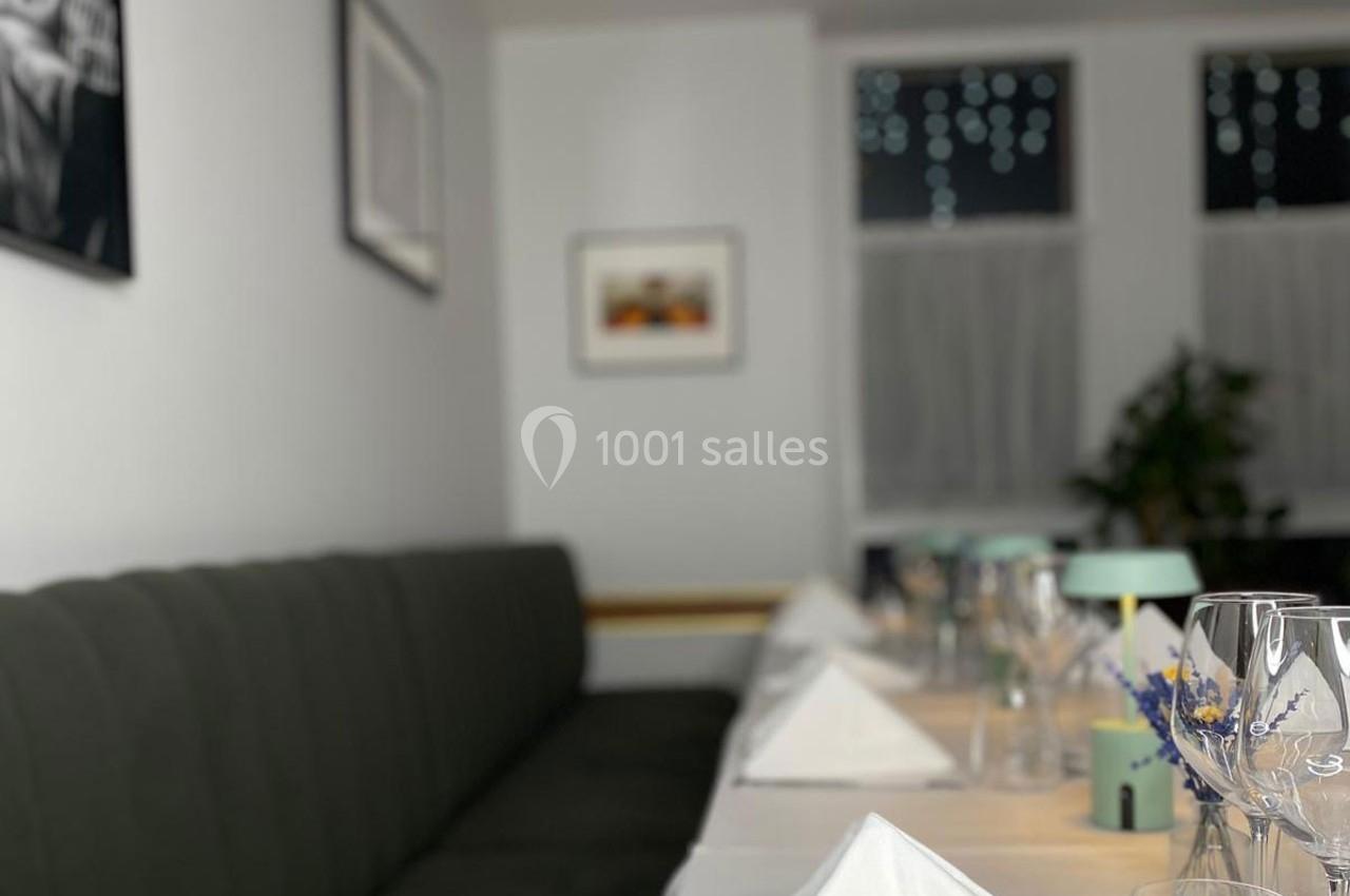 Table dressée avec nappes blanches, verres et serviettes pliées, dans une salle lumineuse avec décor sobre et plantes.