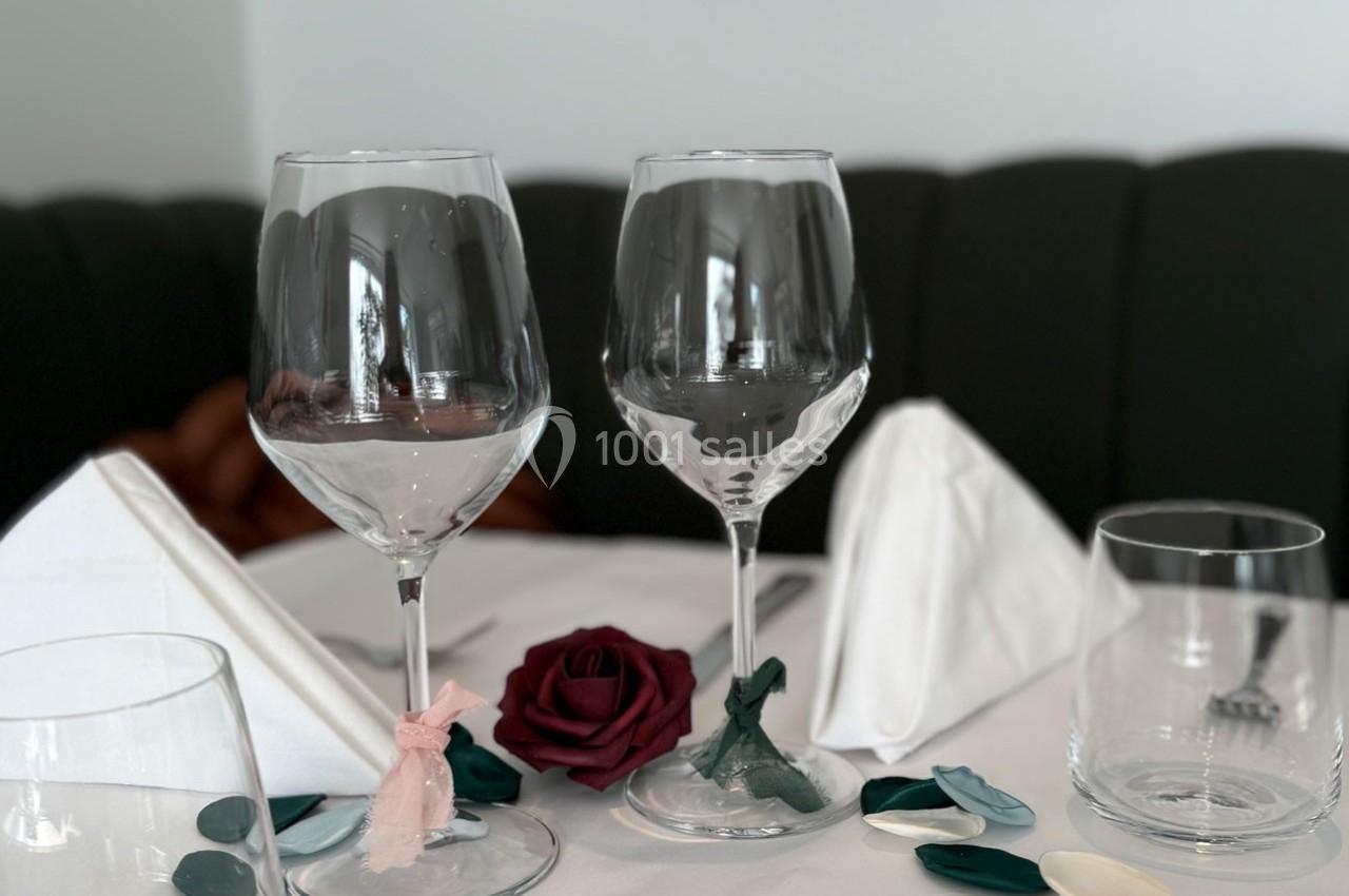 Deux verres à vin décorés de rubans, entourés de pétales et d'une rose rouge sur une table dressée.