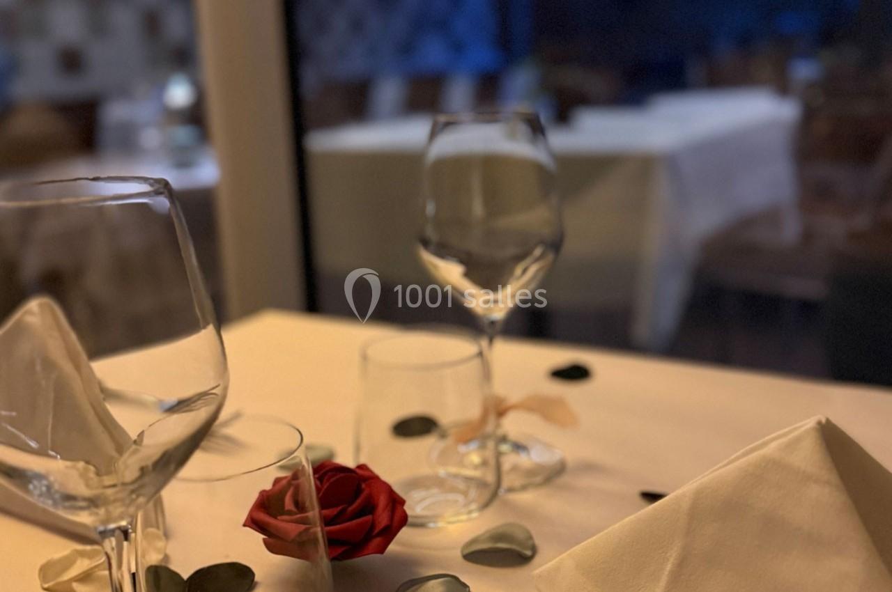 Table élégamment dressée avec une rose rouge, des pétales et des verres, dans un restaurant à l'ambiance tamisée.
