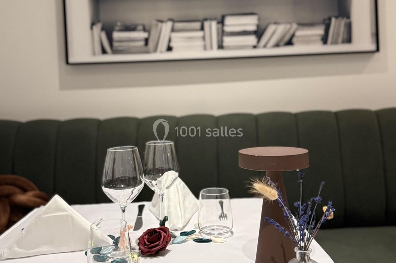 Table dressée avec élégance, décorée de fleurs séchées, verres à vin et serviettes pliées, devant une banquette verte.