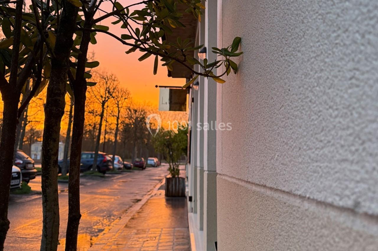Coucher de soleil illuminant une rue bordée d'arbres et de bâtiments, avec des reflets sur le sol mouillé.
