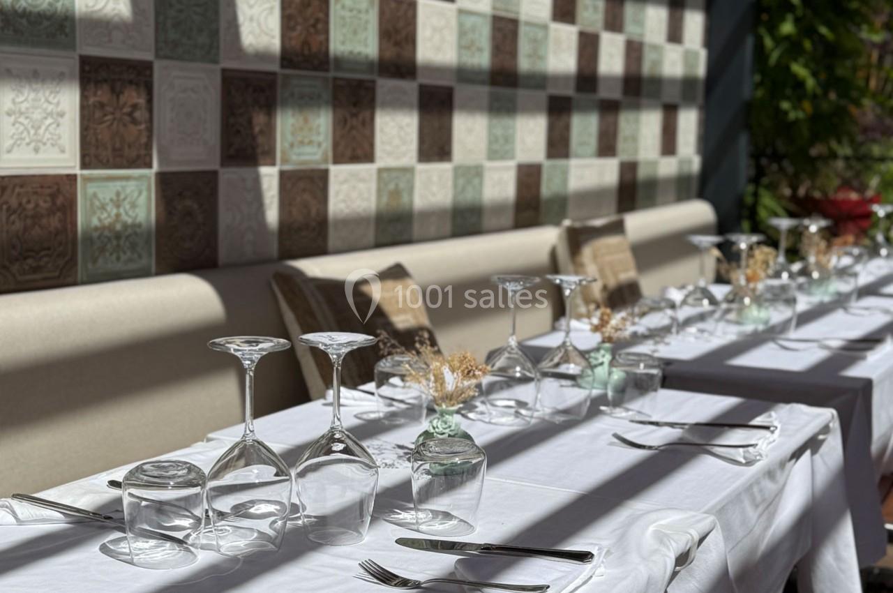 Table dressée avec nappes blanches, verres retournés et couverts, devant un mur décoré de carreaux colorés.