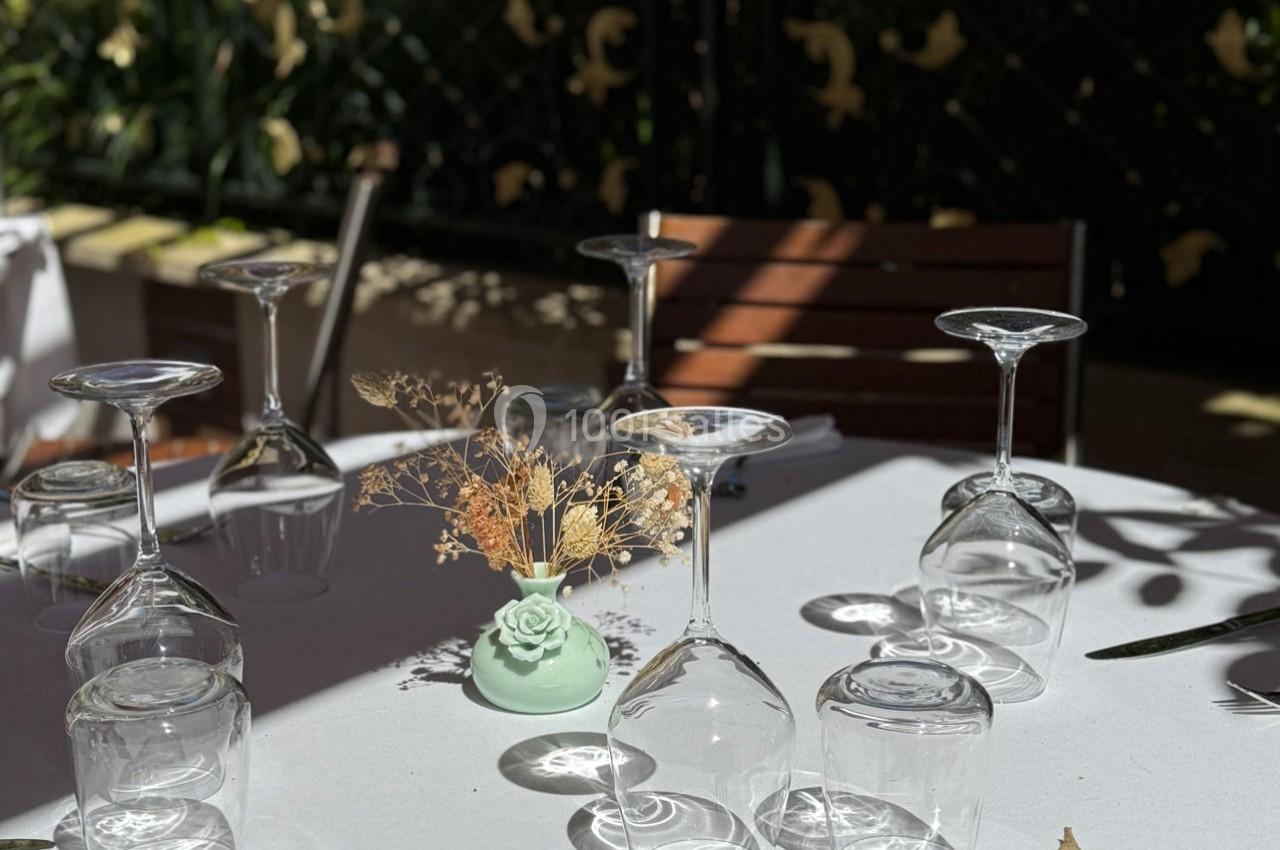 Table dressée avec nappe blanche, verres à pied retournés et petit vase décoratif contenant des fleurs séchées.