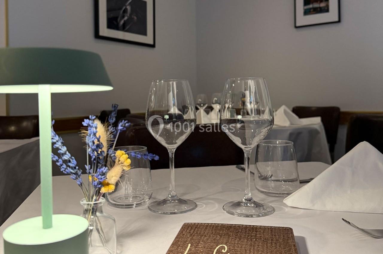 Table dressée avec élégance dans un restaurant, avec verres à vin, serviettes pliées et décoration florale.
