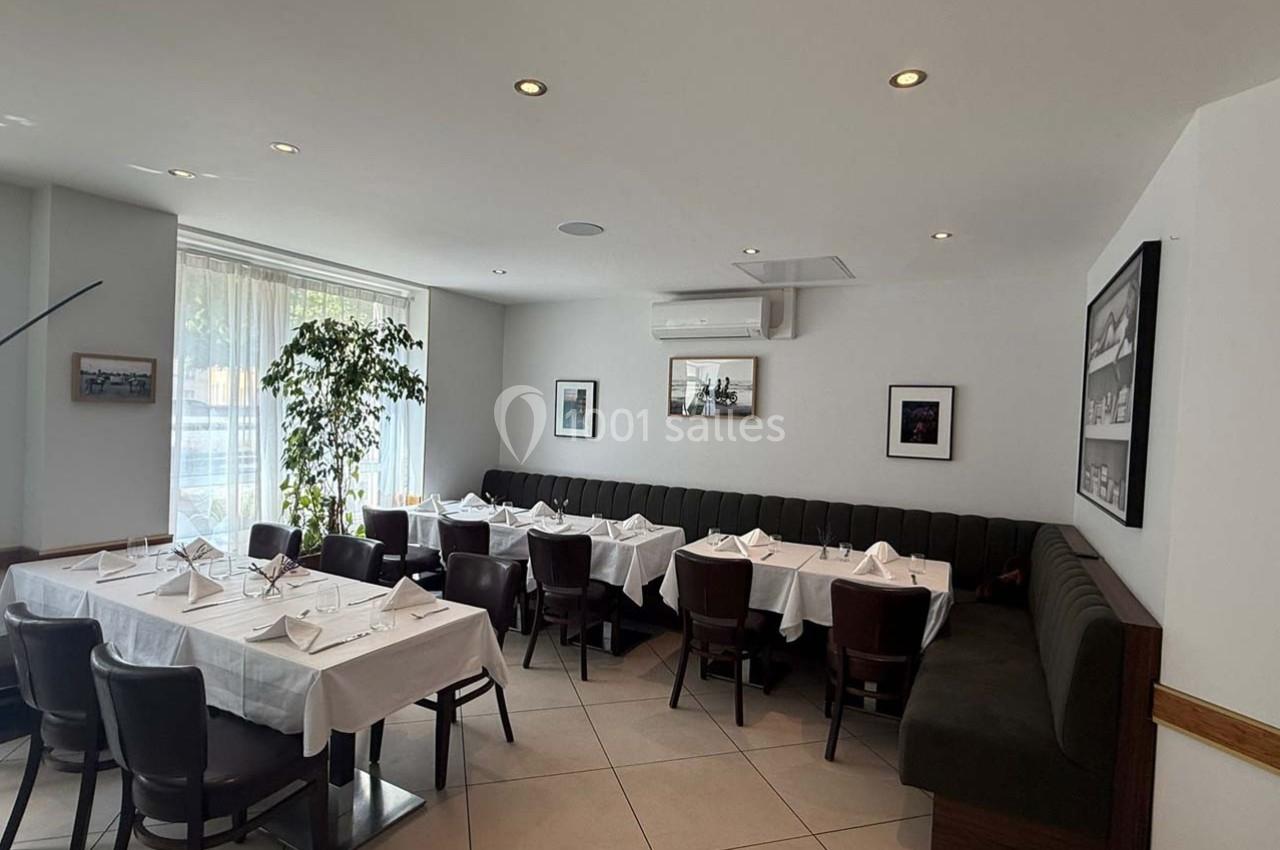 Salle de restaurant lumineuse avec tables dressées, chaises en bois, banquette rembourrée et décorations murales.