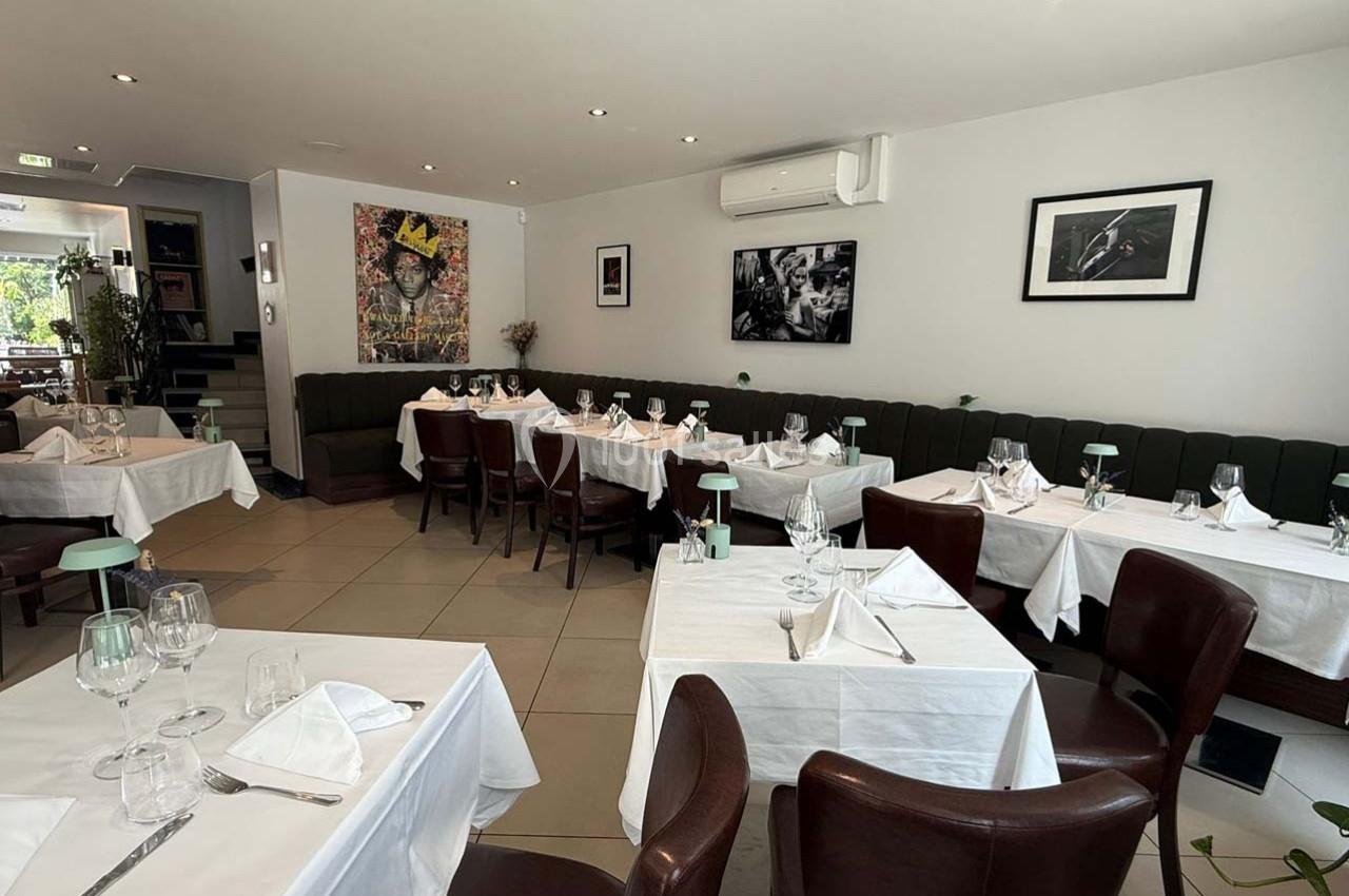 Salle de restaurant élégante avec tables dressées, nappes blanches, chaises en cuir et décorations murales.