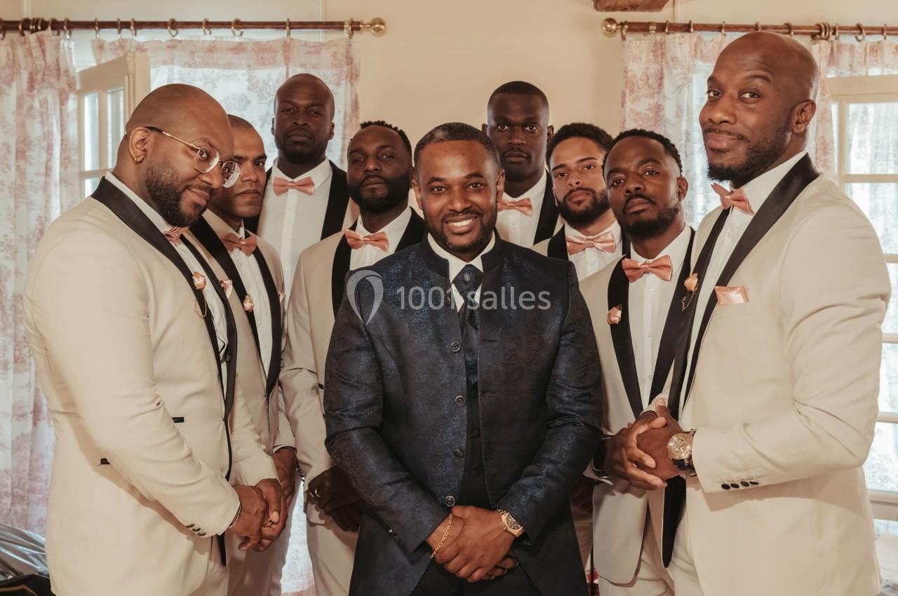 Un groupe d'hommes en costumes élégants, souriant, posant dans une pièce lumineuse avec des rideaux fleuris.