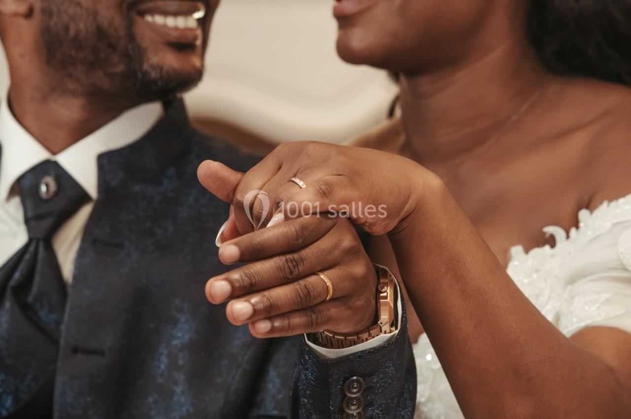 Un couple habillé élégamment se tient la main, mettant en valeur leurs alliances dorées.