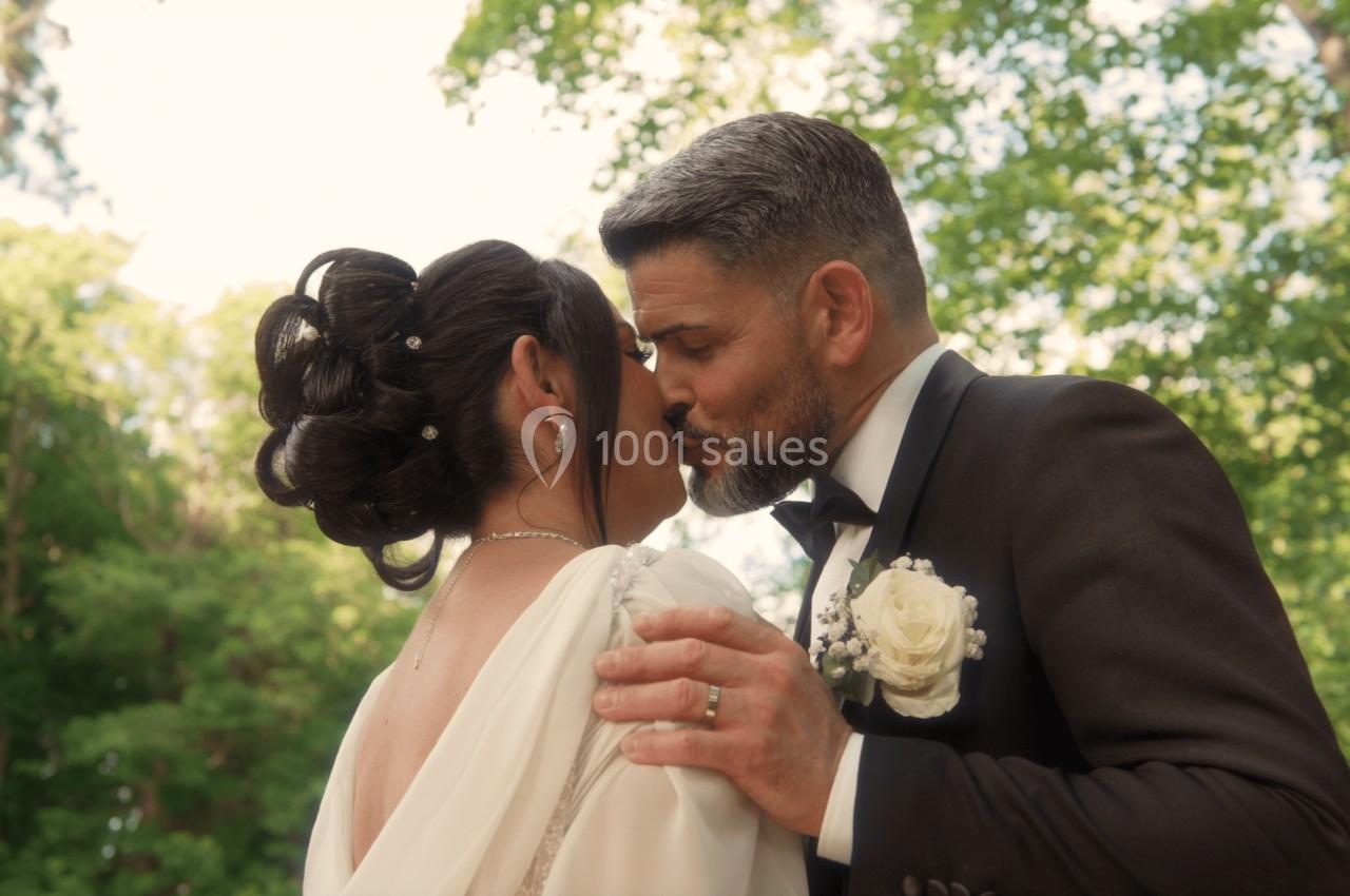 Un couple en tenue de mariage s'embrasse tendrement dans un cadre extérieur verdoyant.