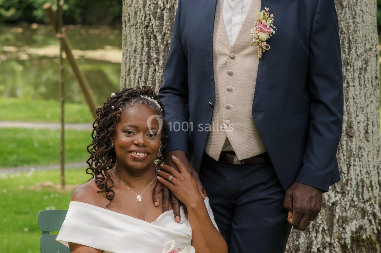 Un couple en tenue de mariage pose devant un grand arbre dans un parc verdoyant.