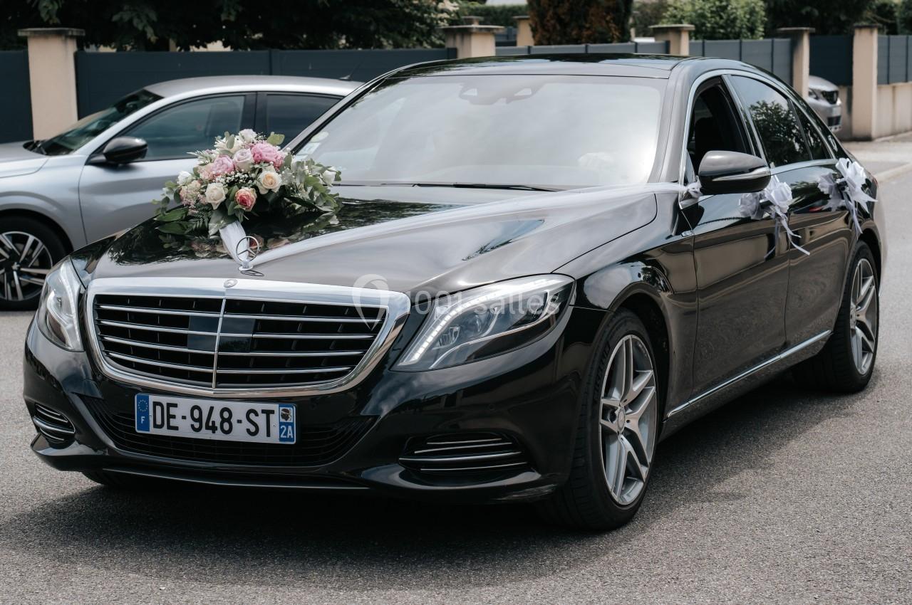 Voiture de cérémonie noire décorée de fleurs sur le capot, stationnée dans une rue résidentielle.
