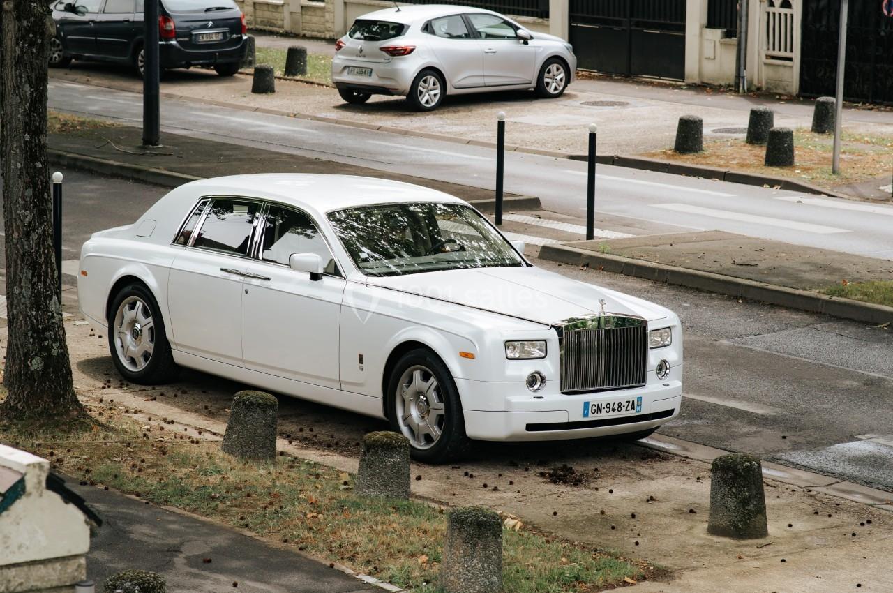Voiture blanche de luxe stationnée sur un trottoir dans une rue résidentielle bordée d'arbres.