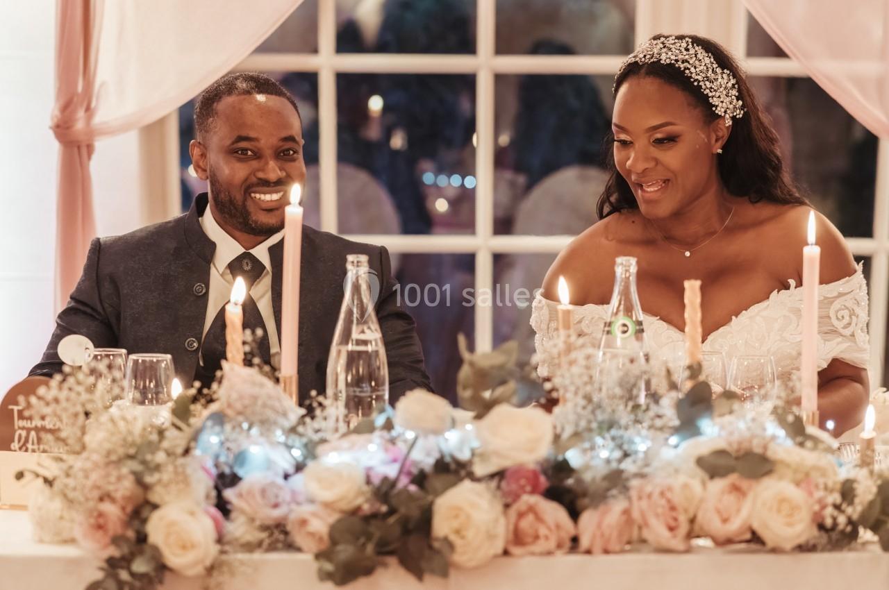 Un couple souriant assis à une table décorée de fleurs et de bougies lors d'une réception.