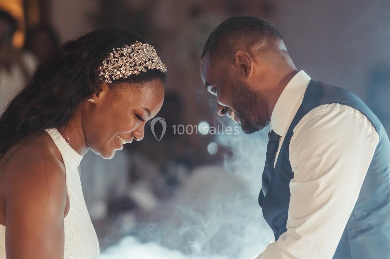 Un couple souriant partage un moment complice dans une ambiance lumineuse et légèrement enfumée.