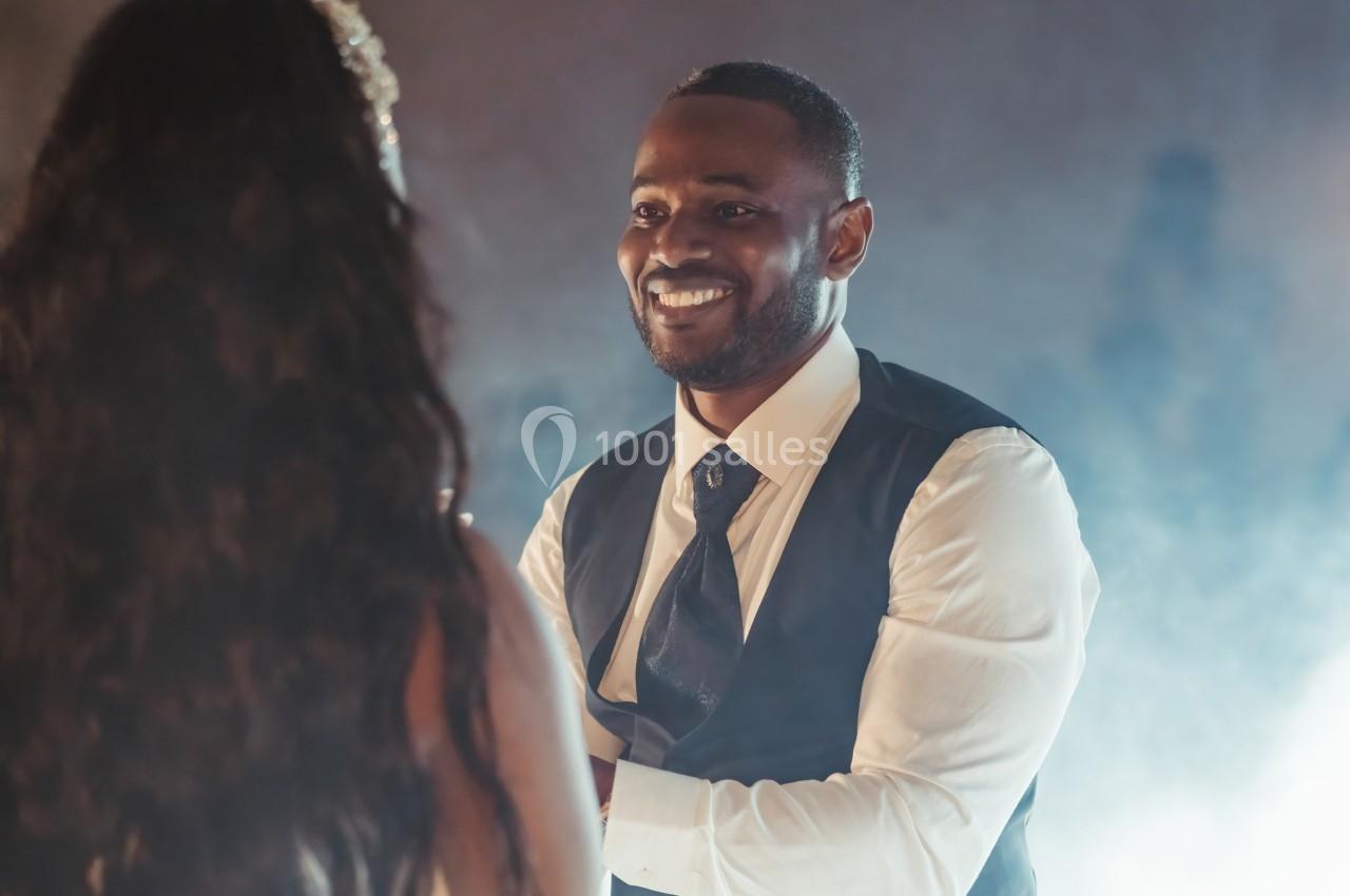 Un homme souriant en costume regarde une femme de dos dans une ambiance lumineuse et légèrement brumeuse.
