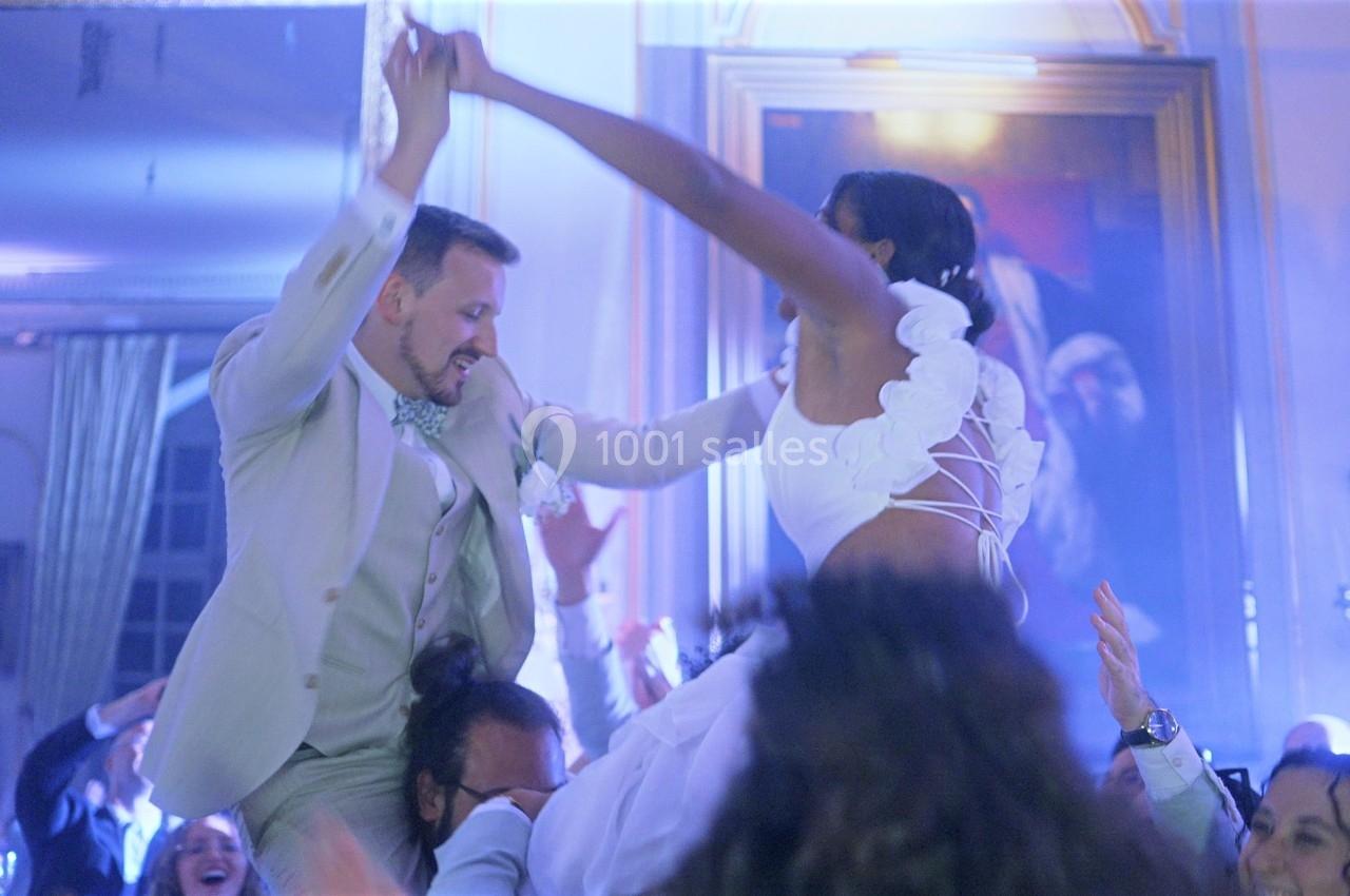 Un couple en tenue de mariage danse joyeusement, entouré d'invités célébrant dans une ambiance festive et lumineuse.