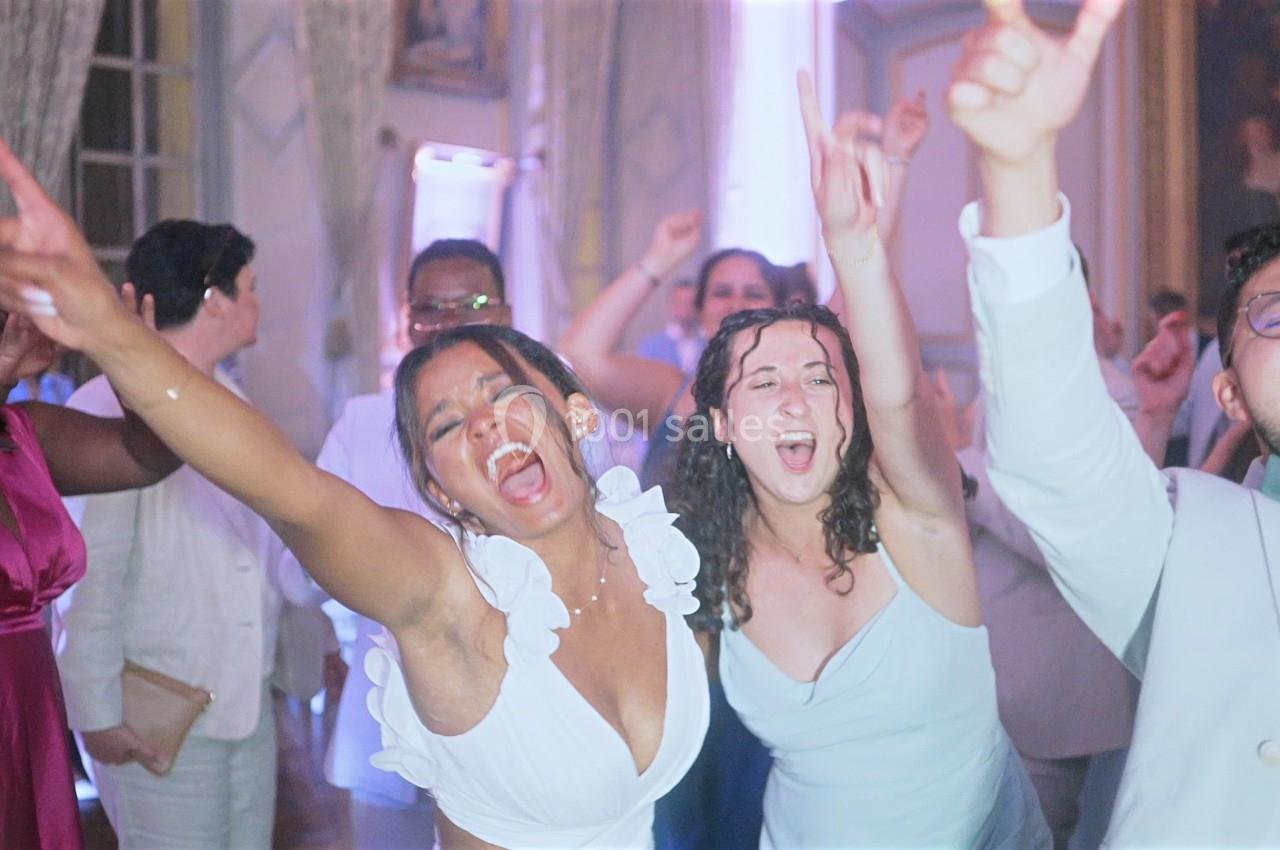 Des personnes dansent et chantent avec enthousiasme lors d'une fête dans une salle éclairée de lumières colorées.