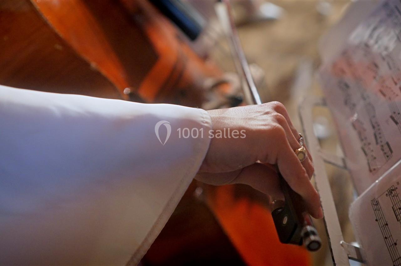 Main jouant du violoncelle avec un archet, près d'une partition musicale éclairée.