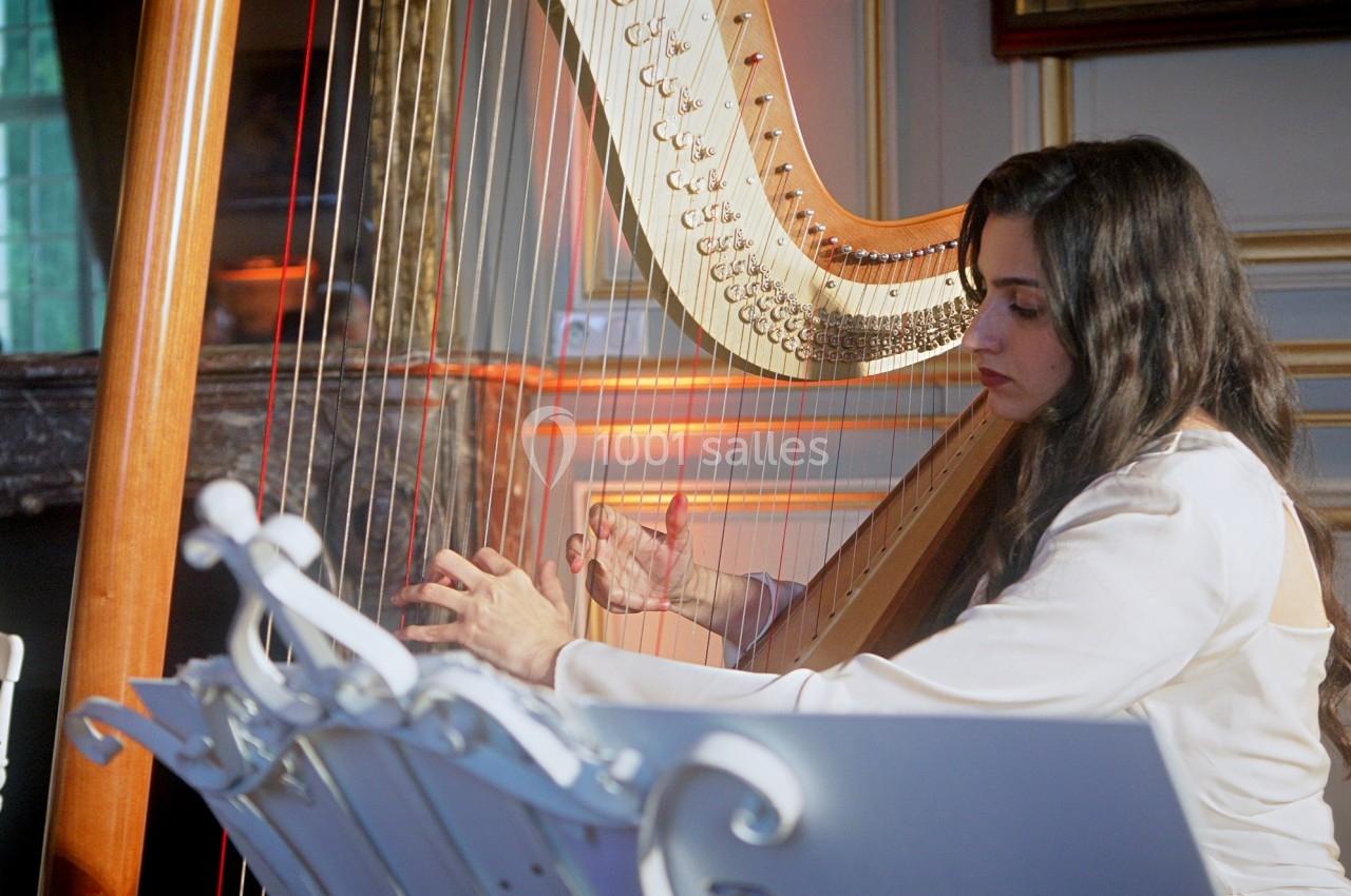 Une musicienne joue de la harpe dans une pièce élégante avec des moulures et un éclairage chaleureux.