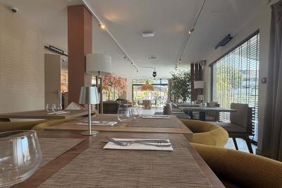 Salle de restaurant lumineuse avec tables dressées, chaises confortables et grandes baies vitrées laissant entrer la lumière…