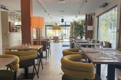 Salle de restaurant lumineuse avec tables dressées, chaises confortables et grandes baies vitrées laissant entrer la lumière…