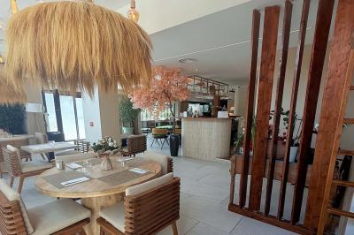 Salle de restaurant lumineuse avec tables dressées, chaises confortables et grandes baies vitrées laissant entrer la lumière…