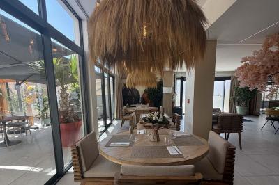 Salle de restaurant lumineuse avec tables dressées, chaises confortables et grandes baies vitrées laissant entrer la lumière…