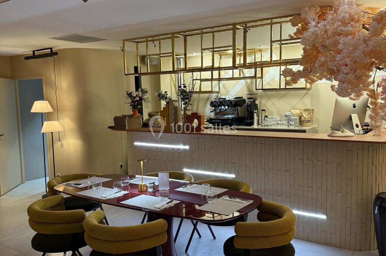 Salle de restaurant avec une table dressée pour quatre personnes, un comptoir moderne et une décoration florale.