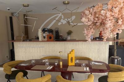 Salle de restaurant élégante avec table dressée, chaises vertes, bar en arrière-plan et décoration florale.