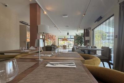 Salle de restaurant élégante avec table dressée, chaises vertes, bar en arrière-plan et décoration florale.