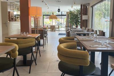Salle de restaurant élégante avec table dressée, chaises vertes, bar en arrière-plan et décoration florale.