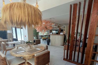 Salle de restaurant élégante avec table dressée, chaises vertes, bar en arrière-plan et décoration florale.