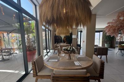 Salle de restaurant élégante avec table dressée, chaises vertes, bar en arrière-plan et décoration florale.
