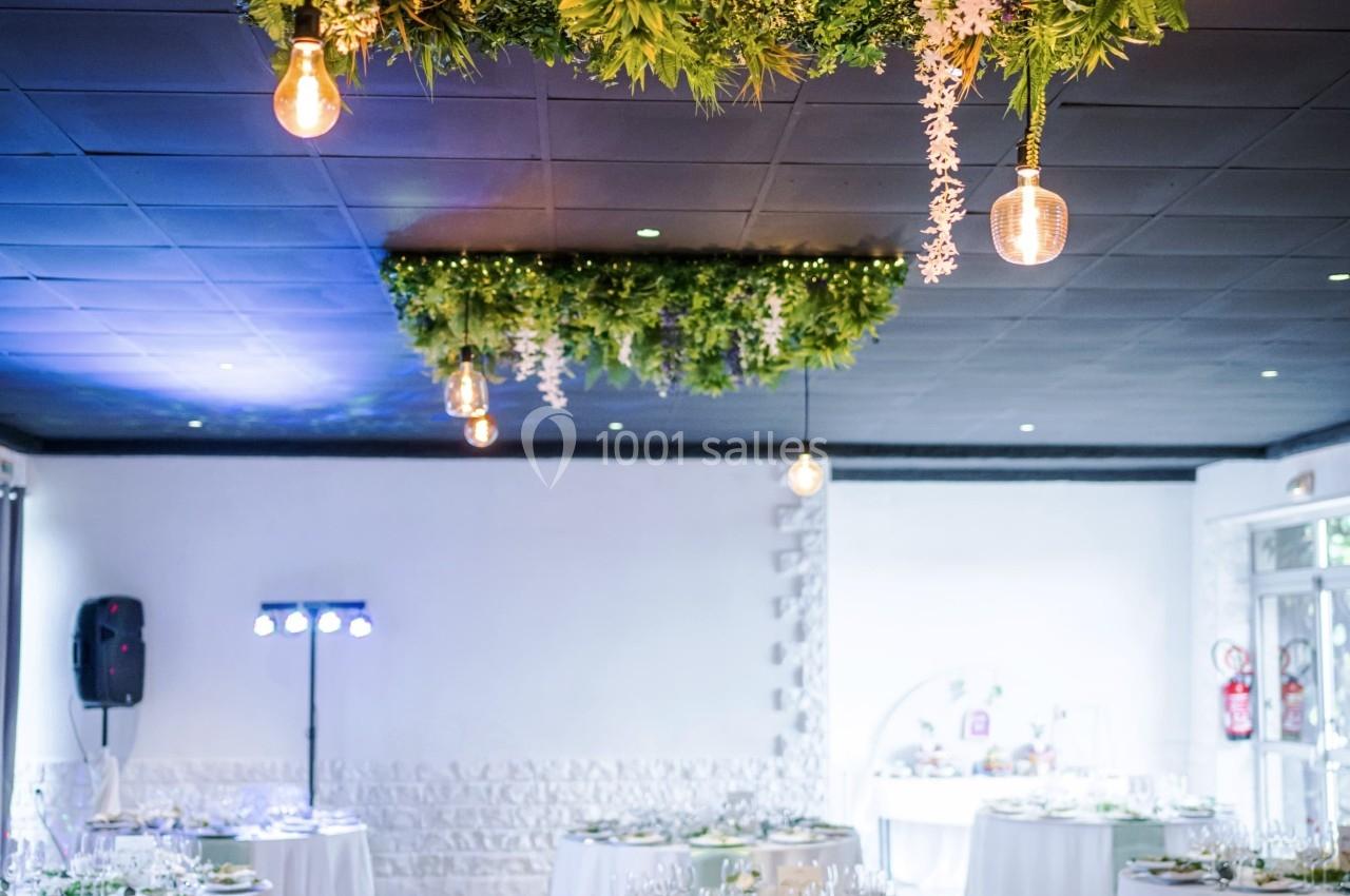 Salle de réception décorée avec des tables dressées et un plafond orné de guirlandes végétales et luminaires suspendus.