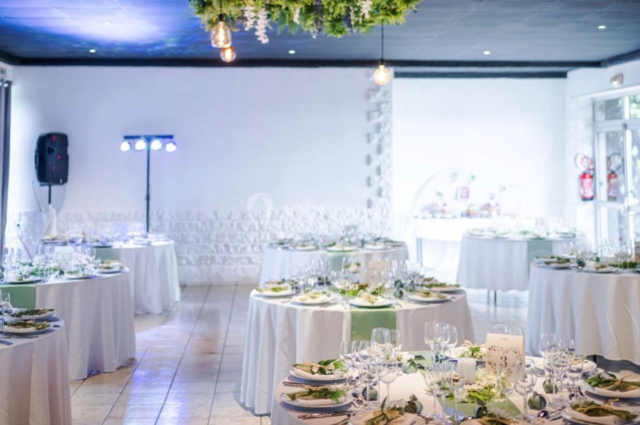 Salle de réception lumineuse avec tables rondes décorées de nappes blanches et centres de table végétaux.