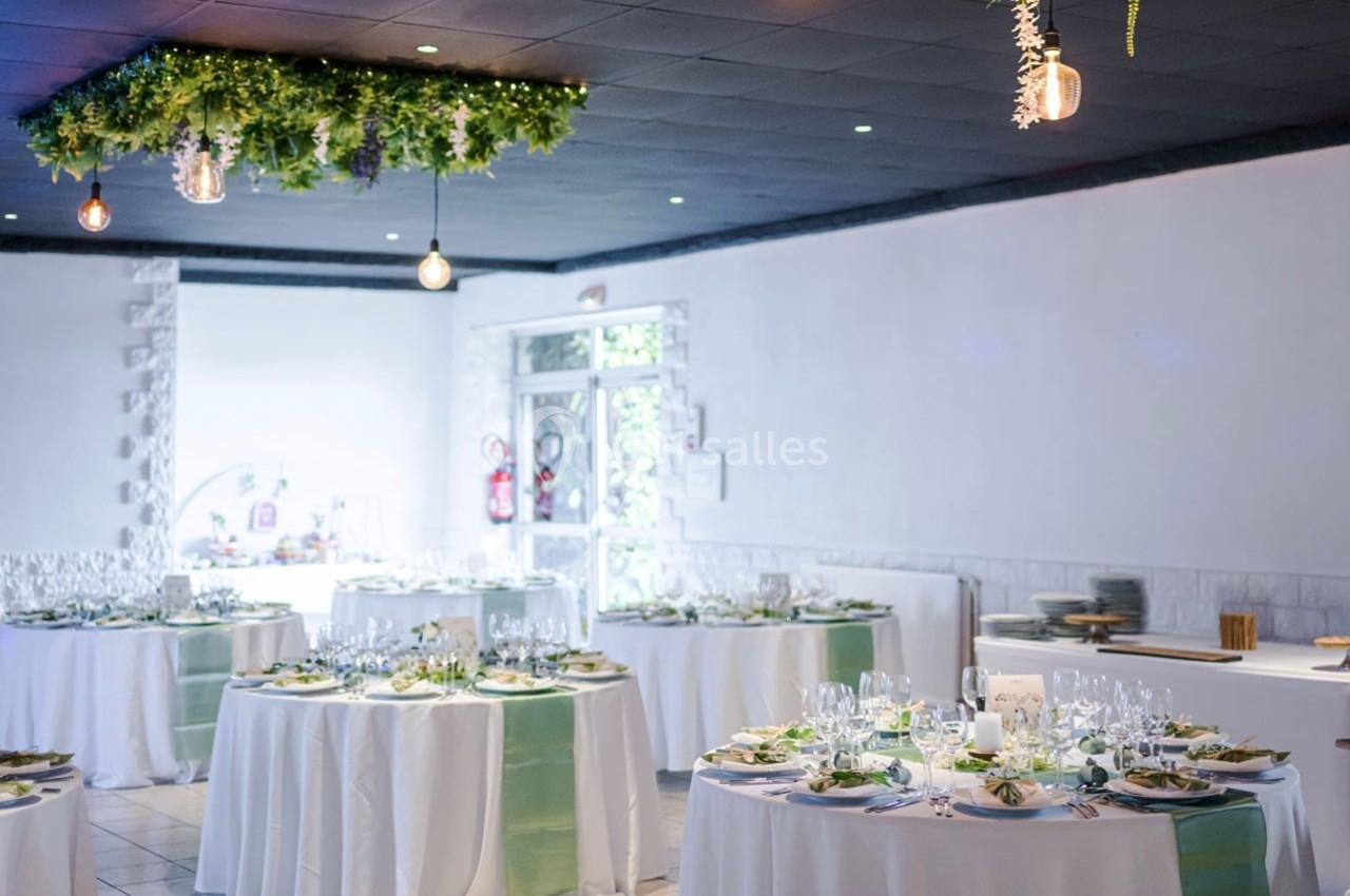 Salle de réception décorée avec des tables rondes dressées, nappes blanches et touches de verdure suspendues.