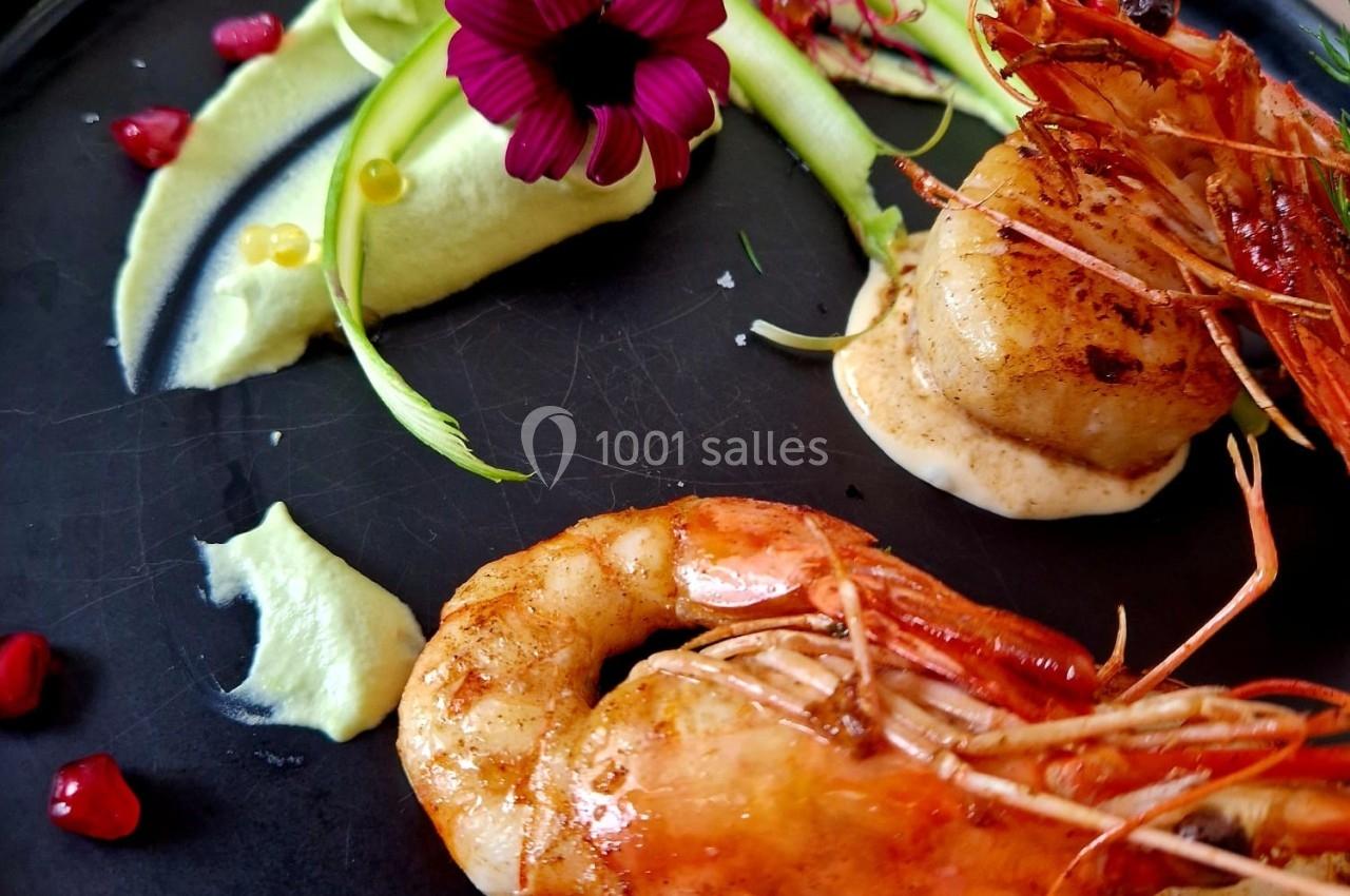 Assiette gastronomique avec crevettes grillées, noix de Saint-Jacques, purée verte, rubans de légumes et fleur comestible.