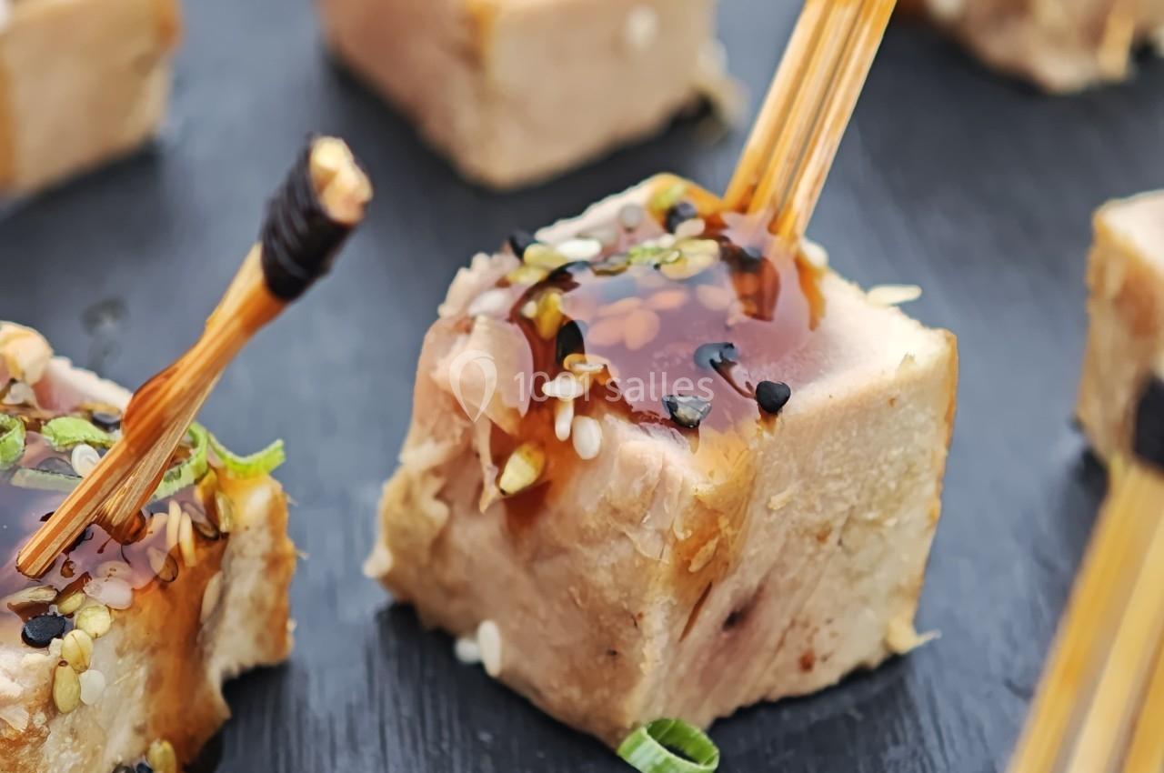 Bouchées de thon mi-cuit surmontées de graines de sésame, ciboulette et sauce, présentées avec des piques en bois.