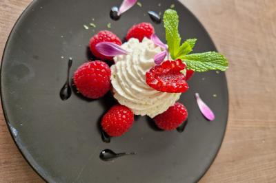 Dessert composé de crème fouettée, framboises fraîches, pétales de fleurs et feuilles de menthe sur une assiette noire.