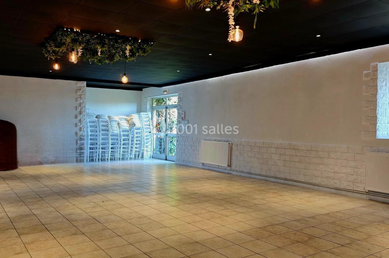 Salle vide avec carrelage beige, murs blancs, plafonds noirs décorés de suspensions végétales et empilement de chaises au…