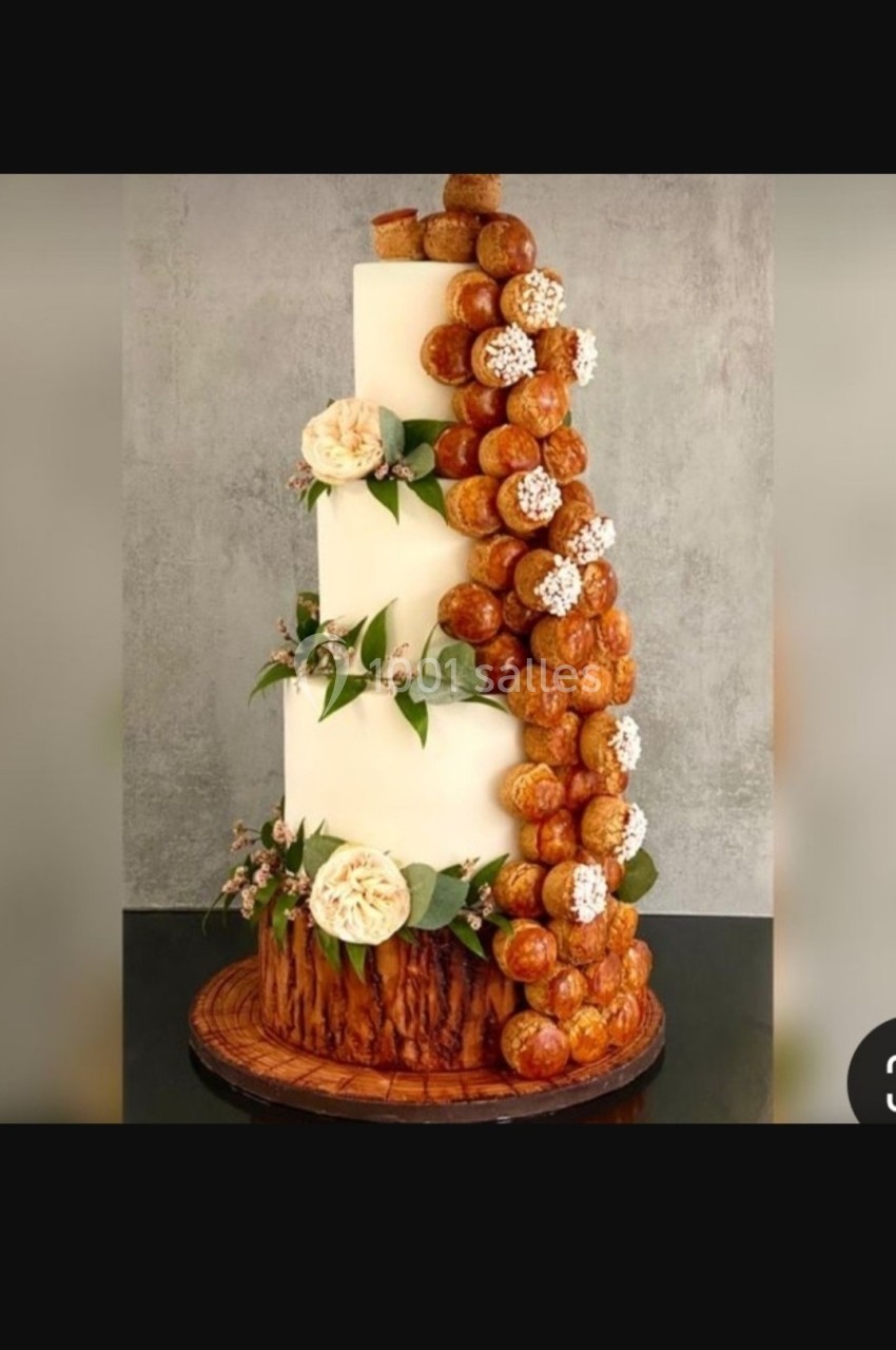 Gâteau de mariage à étages décoré de fleurs blanches, de feuilles vertes et de choux à la crème disposés en cascade.