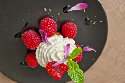 Gâteau décoré de glaçage caramel, éléments en chocolat, framboises et feuilles de menthe sur une assiette blanche.